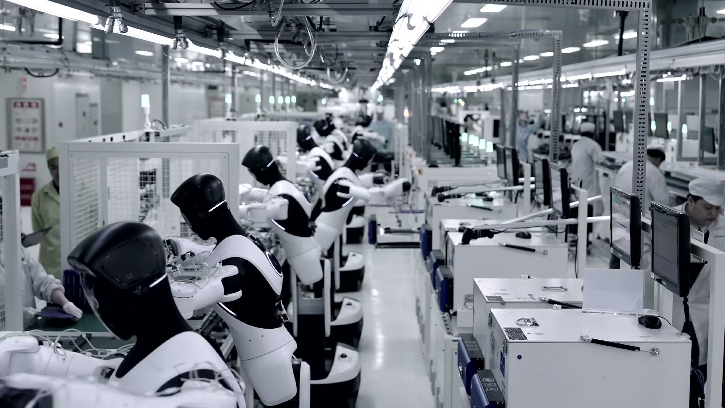 A row of humanoid robots works alongside human operators at stations on a factory assembly line.