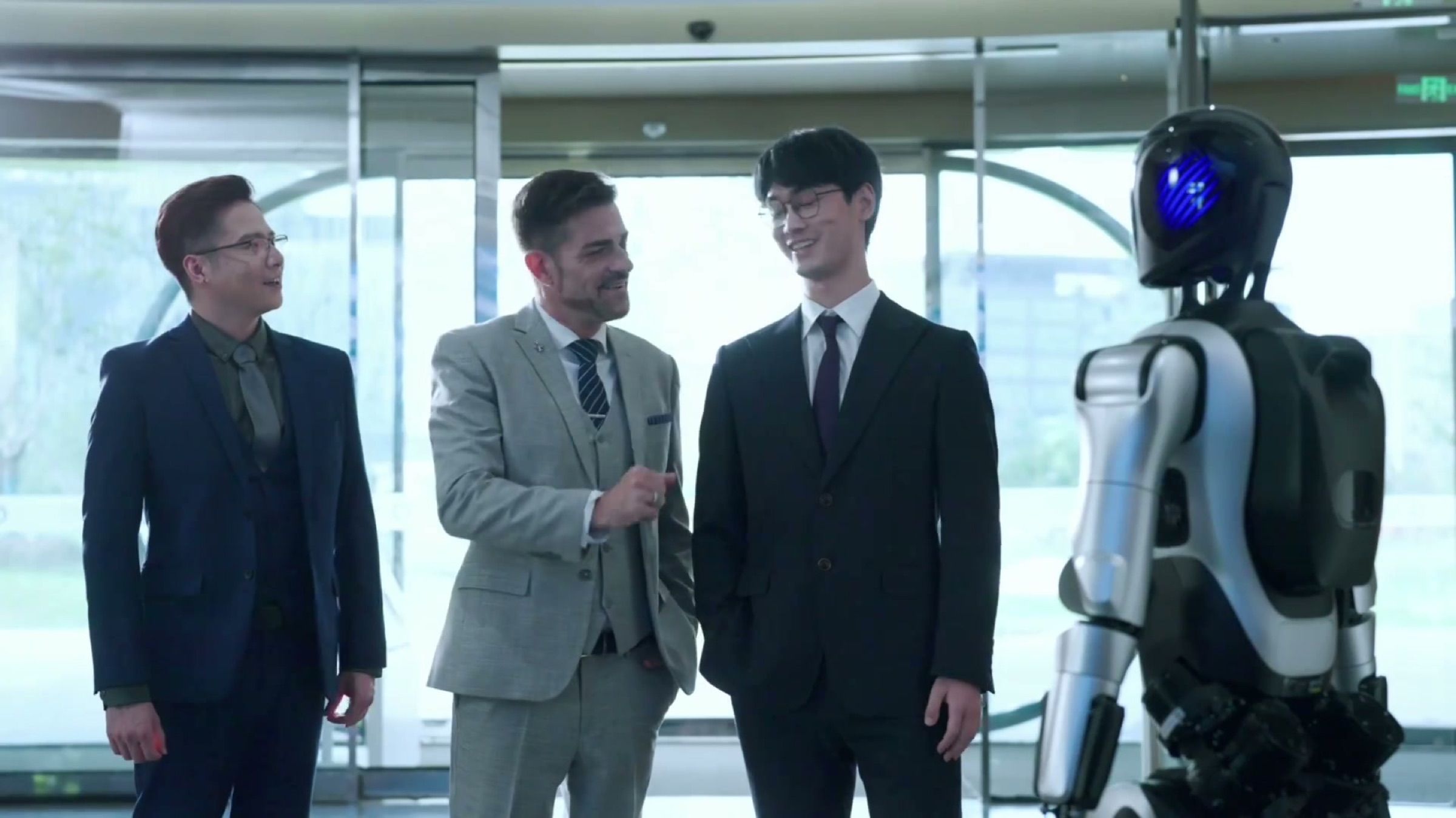 A humanoid robot receives a group of business visitors in a glass-fronted corporate lobby.