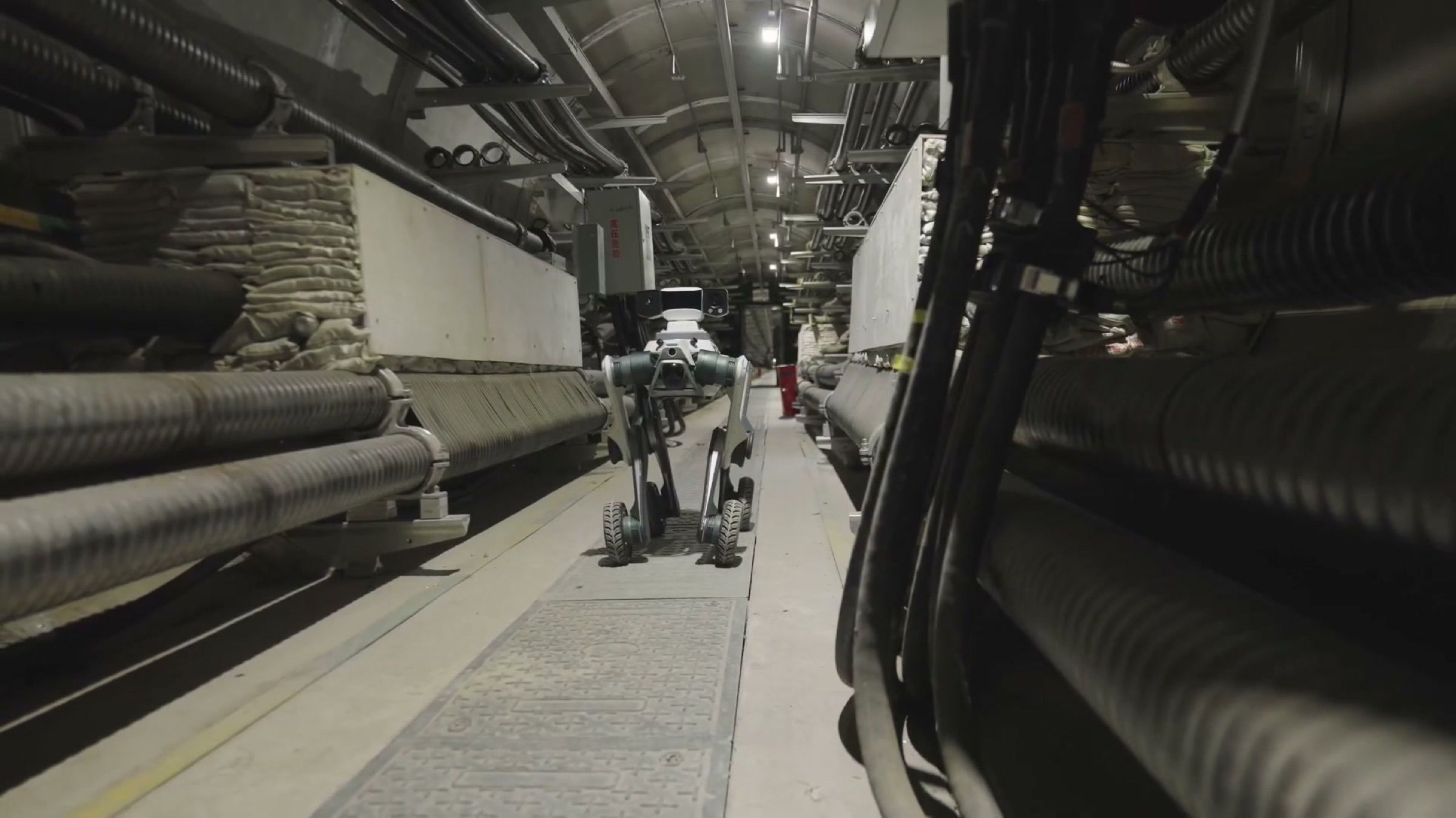 A wheeled-legged robot with an inspection camera patrols a narrow underground power cable tunnel lined with high-voltage cables (frame at 0:24).
