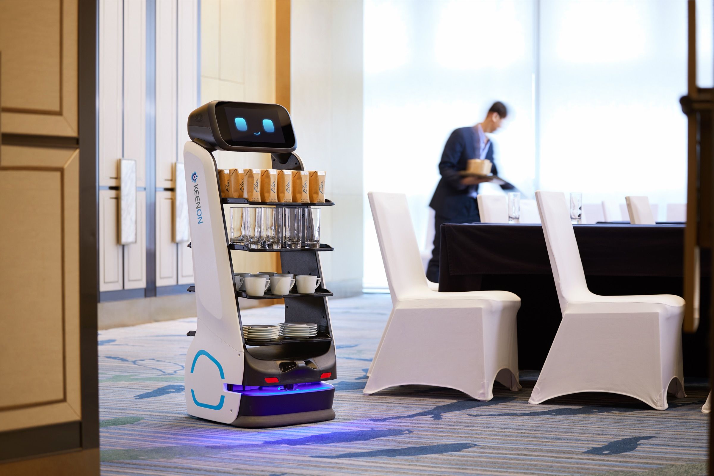 Tray delivery robot in a function room while a staff member sets a table