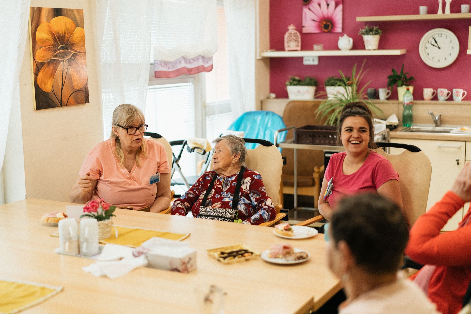 A carer sharing a meal with residents at a table in an aged care dining room