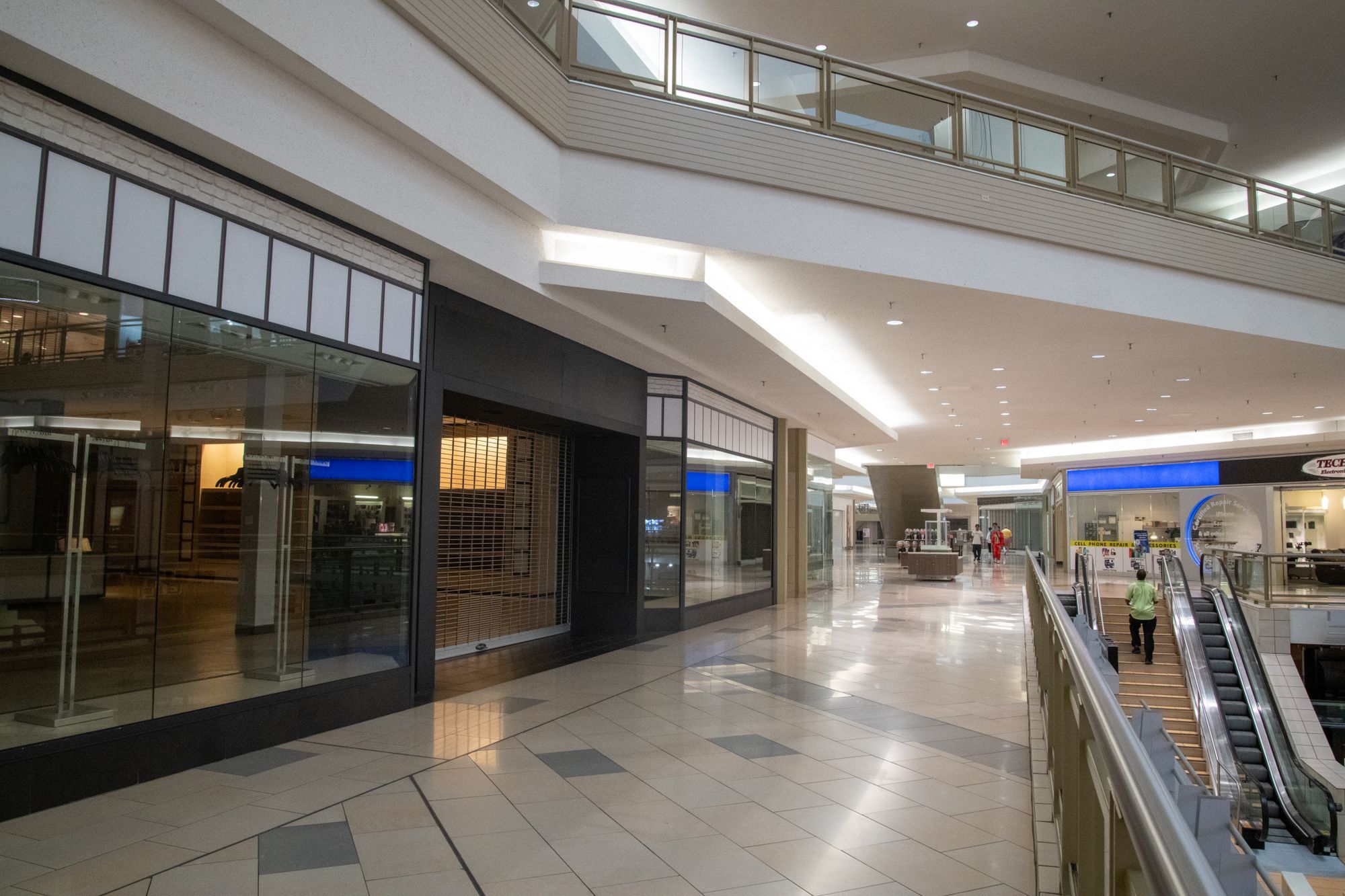 A quiet shopping centre concourse with shopfronts and escalators to the lower level